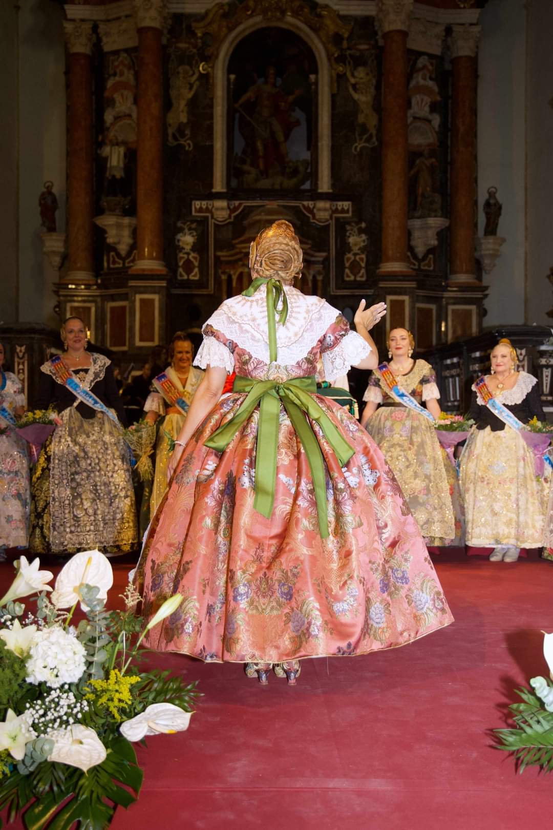 Fallera con traje rosa de espaldas ante el altar de una iglesia