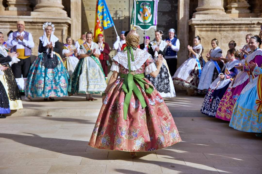 Fallera con traje rosa avanzando entre aplausos en una plaza